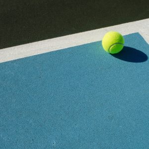 Tennis ball rests on blue tennis court