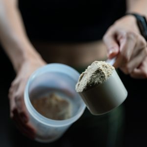 Close up of women with measuring scoop of whey protein and shaker bottle, preparing protein shake.